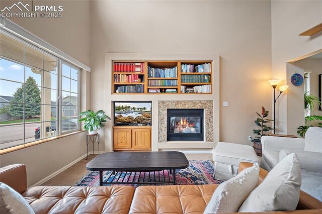 living room with a high ceiling, a glass covered fireplace, baseboards, and carpet