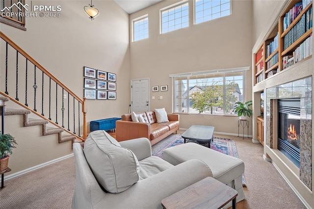 carpeted living room with baseboards, a glass covered fireplace, a towering ceiling, and stairway