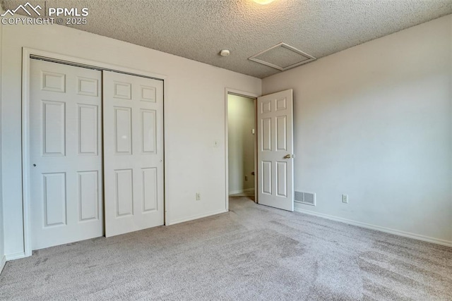 unfurnished bedroom with a textured ceiling, carpet, attic access, visible vents, and a closet