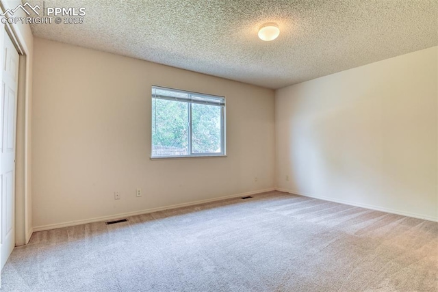 carpeted empty room featuring a textured ceiling, visible vents, and baseboards