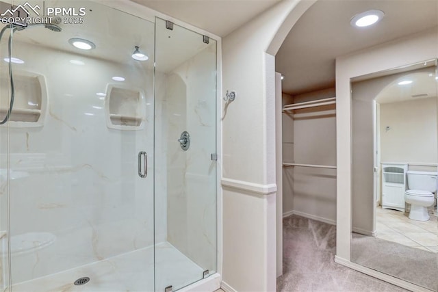 bathroom featuring a walk in closet, toilet, a marble finish shower, baseboards, and visible vents
