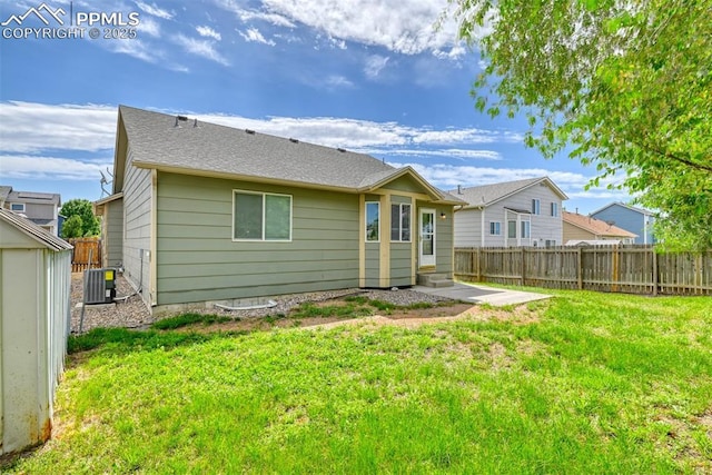 back of house with central AC, a fenced backyard, a shingled roof, entry steps, and a yard