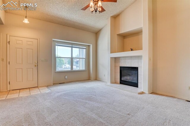 unfurnished living room with a ceiling fan, a fireplace, a textured ceiling, tile patterned floors, and carpet flooring