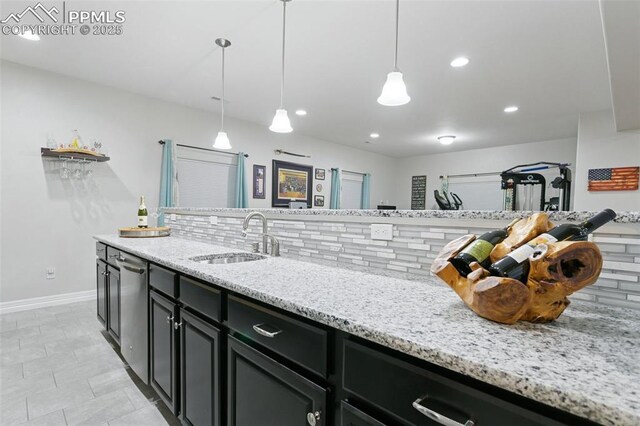 kitchen with a sink, baseboards, dark cabinetry, and light stone countertops
