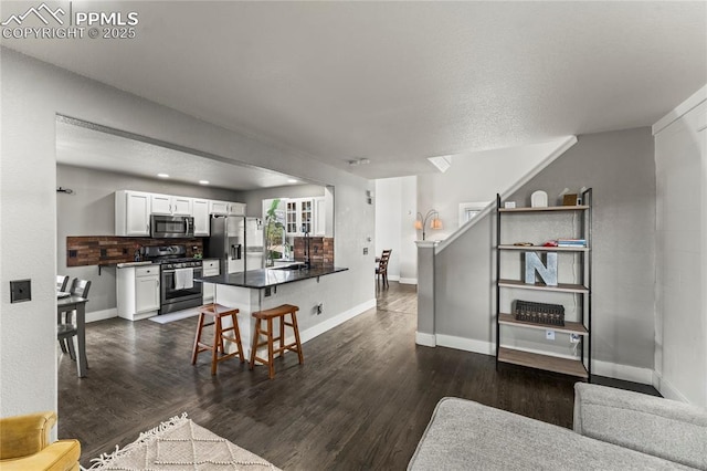 interior space featuring a kitchen bar, dark countertops, appliances with stainless steel finishes, white cabinets, and a peninsula