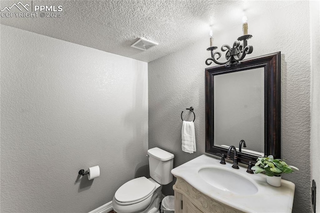bathroom featuring a textured ceiling, visible vents, vanity, toilet, and a textured wall