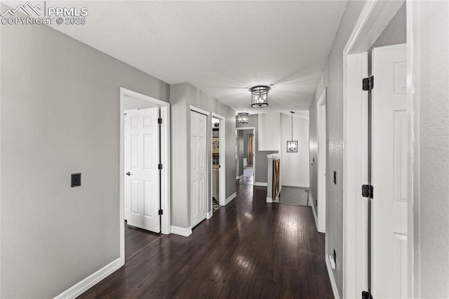 hall featuring baseboards, a textured wall, dark wood-style flooring, and a textured ceiling
