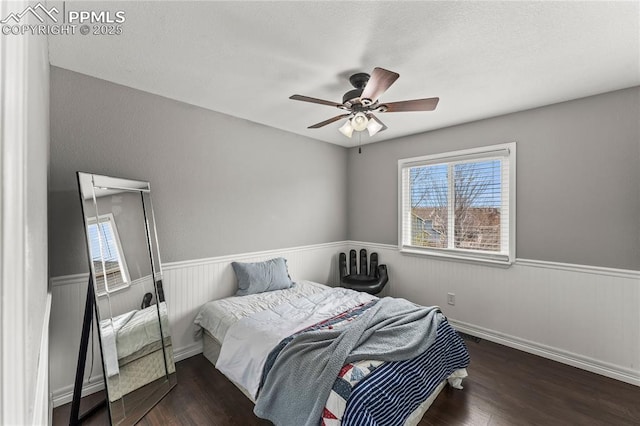 bedroom featuring wood finished floors, ceiling fan, and a wainscoted wall
