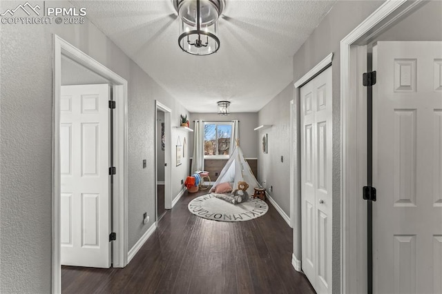 hall featuring a textured ceiling, a textured wall, baseboards, and hardwood / wood-style floors