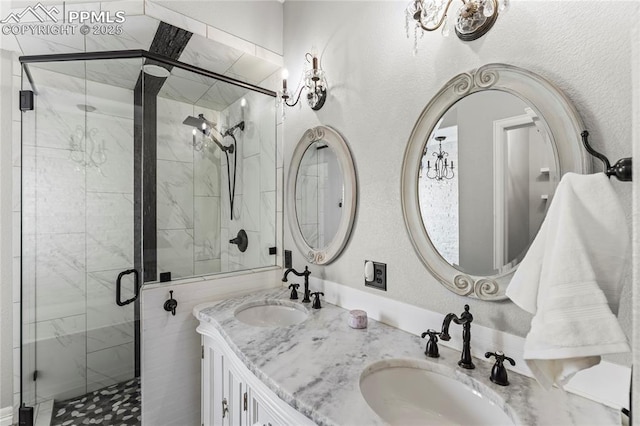 full bath featuring a sink, an inviting chandelier, a stall shower, and double vanity