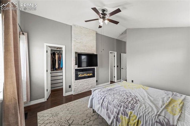 bedroom with ceiling fan, a stone fireplace, baseboards, dark wood-type flooring, and a spacious closet