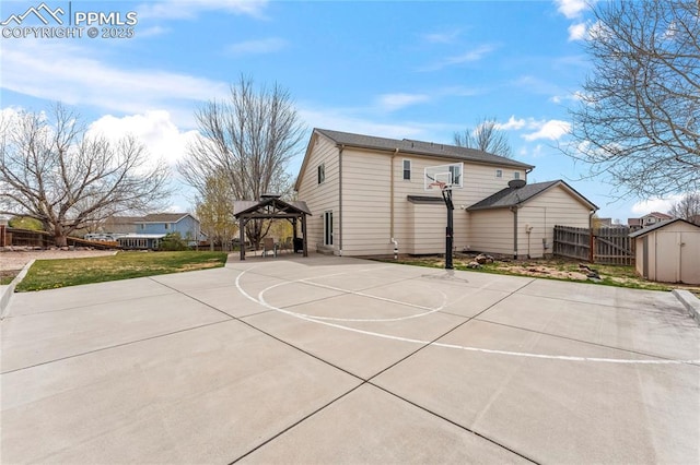view of basketball court featuring basketball hoop, fence, a gazebo, and a shed