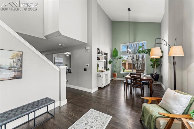 living room featuring high vaulted ceiling, ceiling fan with notable chandelier, baseboards, wood finished floors, and stairway