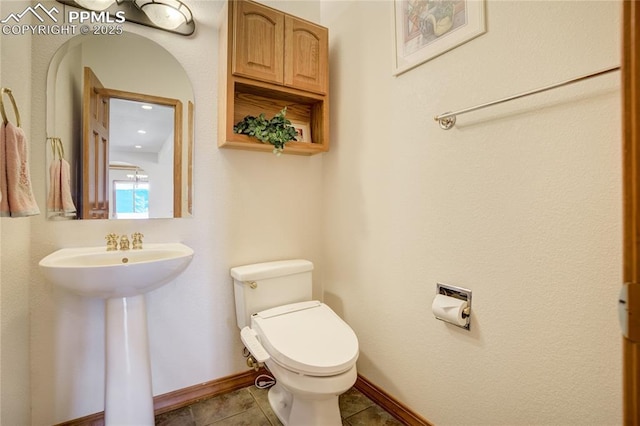 half bathroom with toilet, a sink, baseboards, and tile patterned flooring