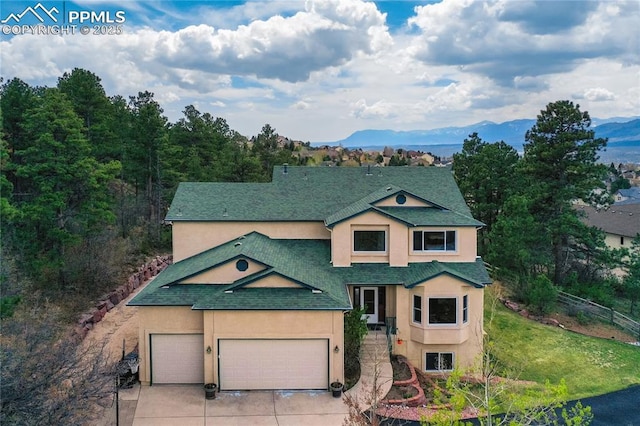 view of front of property with roof with shingles, stucco siding, driveway, a mountain view, and a garage