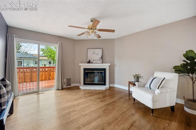 6277 Gunshot Pass Dr, Colorado Springs, CO 80917 - living area featuring wood finished floors, a ceiling fan, a glass covered fireplace, a textured ceiling, and baseboards