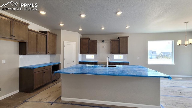 10630 Wolf Lake Dr, Colorado Springs, CO 80924 - kitchen featuring baseboards, backsplash, a center island with sink, a textured ceiling, and a sink