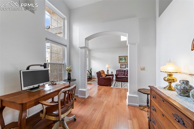 office space featuring arched walkways, baseboards, and light wood-style flooring