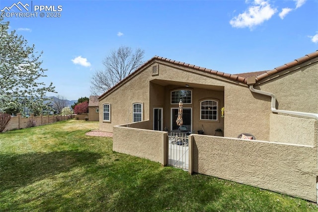 rear view of house featuring a fenced backyard, stucco siding, a gate, a tiled roof, and a lawn