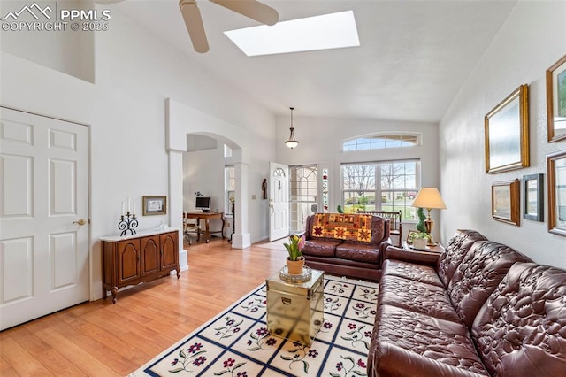living room featuring a skylight, arched walkways, light wood-type flooring, and high vaulted ceiling