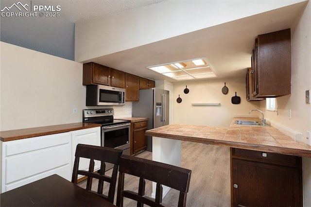 1950 Rusty Hinge Dr, Colorado Springs, CO 80920 - kitchen featuring appliances with stainless steel finishes, a sink, light wood-style flooring, a peninsula, and tile counters