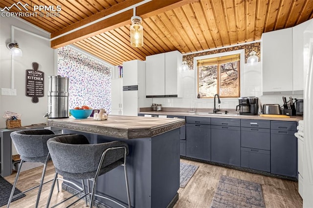 kitchen with gray cabinets, wooden ceiling, a sink, and a kitchen bar