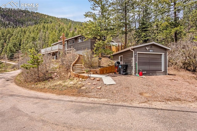 view of side of property with a deck, an outbuilding, a garage, a view of trees, and stairs