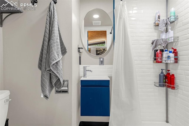 full bathroom featuring vanity, toilet, tiled shower, and visible vents