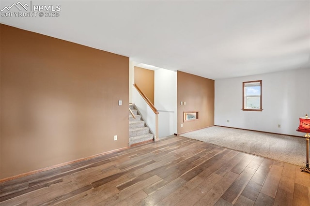 unfurnished living room featuring stairs, hardwood / wood-style flooring, and baseboards