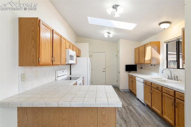 kitchen featuring a peninsula, white appliances, light wood-type flooring, a sink, and backsplash