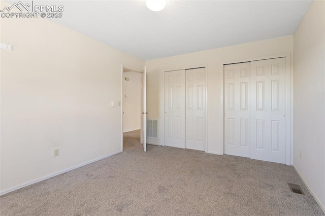 unfurnished bedroom featuring visible vents, baseboards, carpet, and two closets