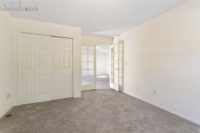 unfurnished bedroom featuring french doors, a textured ceiling, baseboards, a closet, and carpet