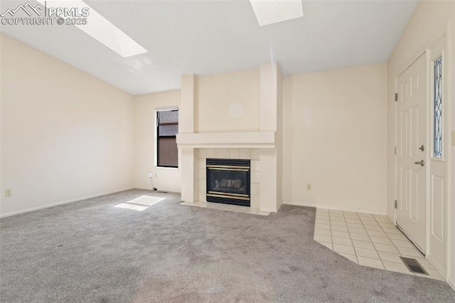 unfurnished living room with carpet flooring, a tiled fireplace, baseboards, a skylight, and visible vents