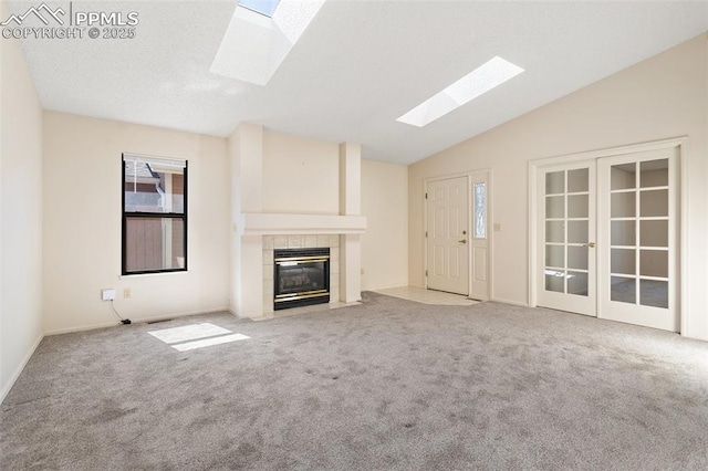 unfurnished living room featuring baseboards, carpet, lofted ceiling with skylight, and a tile fireplace