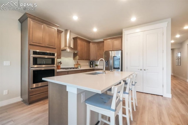 kitchen featuring a sink, stainless steel appliances, light wood finished floors, and wall chimney exhaust hood