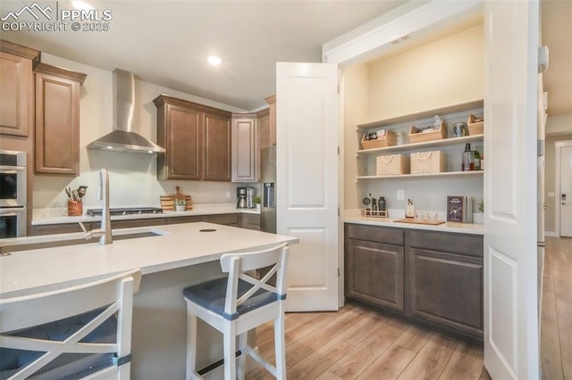 kitchen featuring wall chimney range hood, a breakfast bar area, light wood finished floors, and light countertops