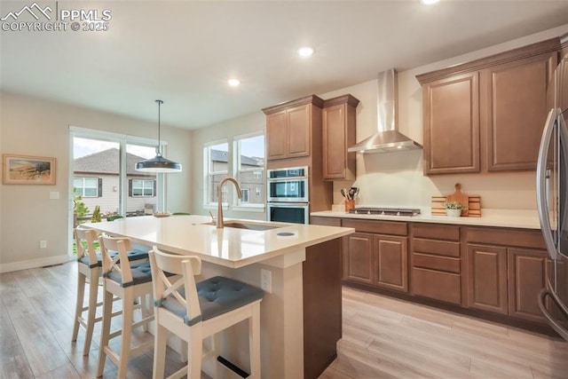 kitchen with wall chimney range hood, a sink, stainless steel appliances, recessed lighting, and light wood-type flooring