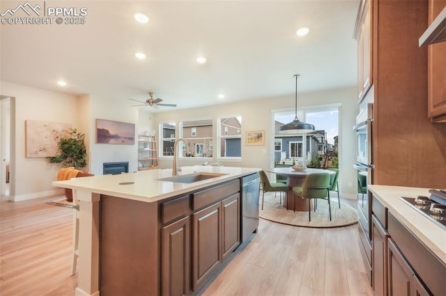 kitchen featuring appliances with stainless steel finishes, a tiled fireplace, a sink, and light wood-style floors