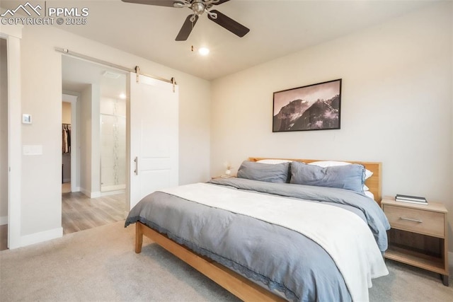 bedroom featuring carpet flooring, ceiling fan, a barn door, ensuite bath, and baseboards