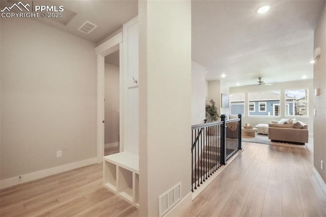 corridor featuring baseboards, visible vents, wood finished floors, and an upstairs landing
