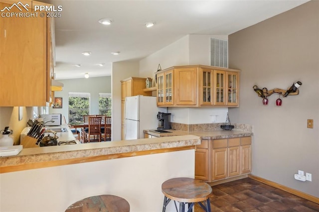 kitchen featuring a breakfast bar, freestanding refrigerator, a peninsula, baseboards, and glass insert cabinets