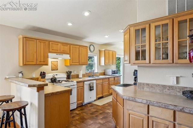kitchen featuring a breakfast bar area, a peninsula, glass insert cabinets, under cabinet range hood, and white appliances