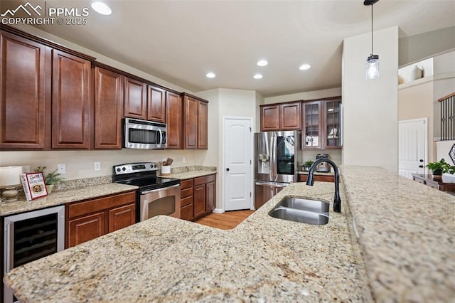 kitchen featuring wine cooler, light stone counters, a sink, light wood-style flooring, and appliances with stainless steel finishes