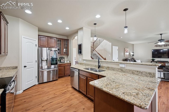 kitchen with a sink, open floor plan, arched walkways, light wood finished floors, and appliances with stainless steel finishes