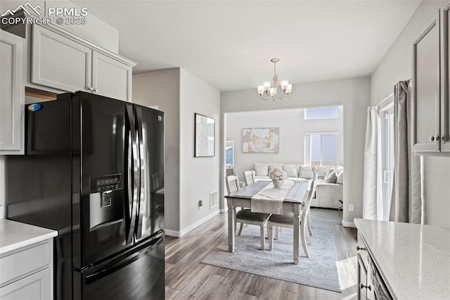 kitchen with baseboards, light stone counters, a chandelier, light wood-style floors, and black fridge