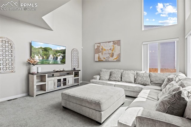 living area with carpet floors, baseboards, visible vents, and a towering ceiling