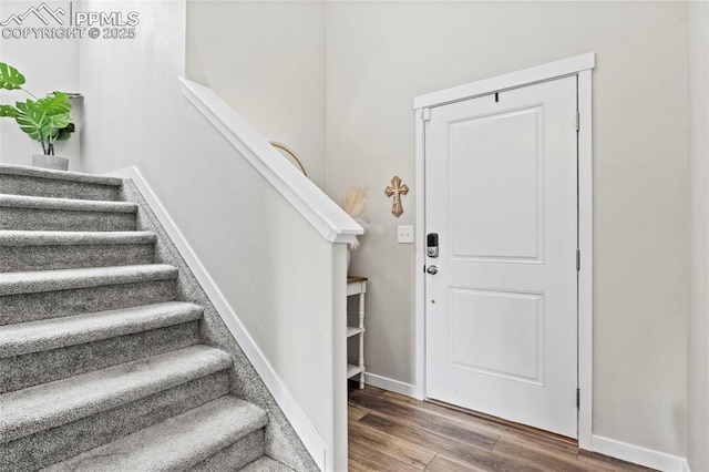 foyer featuring baseboards, wood finished floors, and stairway