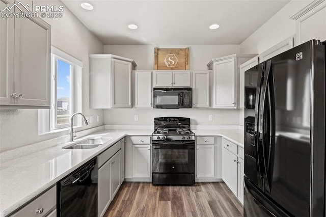 kitchen featuring recessed lighting, a sink, wood finished floors, and black appliances