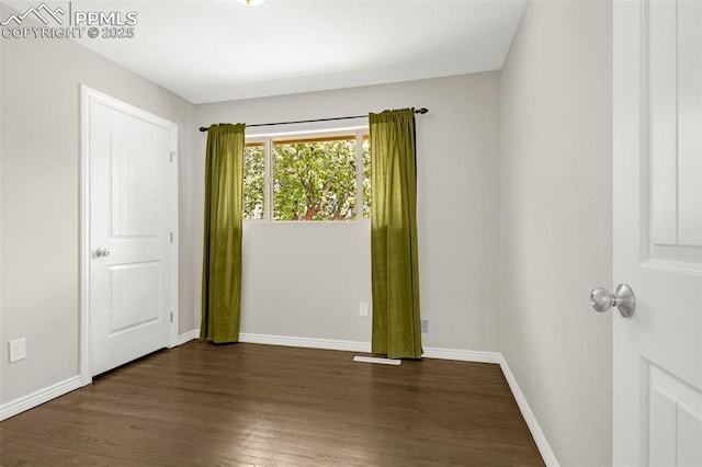 spare room featuring baseboards and dark wood-style floors