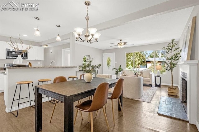 dining room with baseboards, a fireplace with flush hearth, wood finished floors, and ceiling fan with notable chandelier